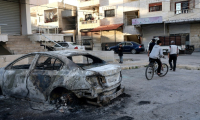 Un jeune fait du vélo à côté d'une voiture détruite après les affrontements entre les nouvelles autorités syriennes et les partisans du président déchu Bachar al-Assad dans la ville de Jableh, dans la province côtière de Lattaquié, le 10 mars 2025 ( AFP / Omar HAJ KADOUR )